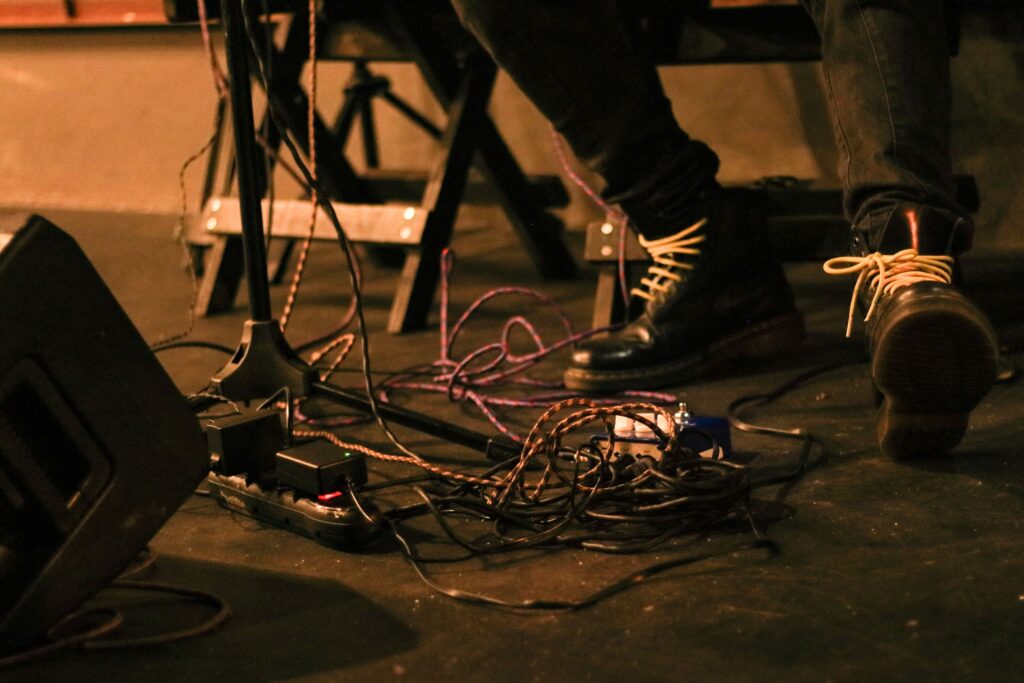Close-up of a musician's feet on stage surrounded by cables and audio equipment.